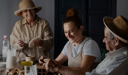 Family gathered around a table; a smiling woman slices food while older relatives look on cheerfully.