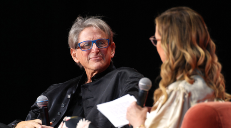Relationship therapist Terry Real smiling and holding a microphone while being interviewed on stage.