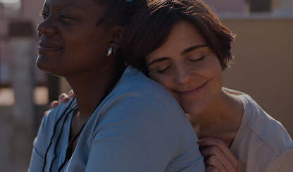 Two women embracing closely outdoors with their eyes closed, smiling softly.